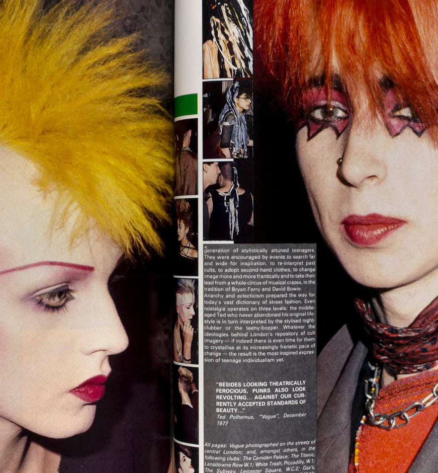 A printed magazine or book page showing a close-up fashion portrait of a person with bright yellow hair, pale makeup, red lipstick, and dark eye makeup, alongside smaller inset photos and text on the right side.