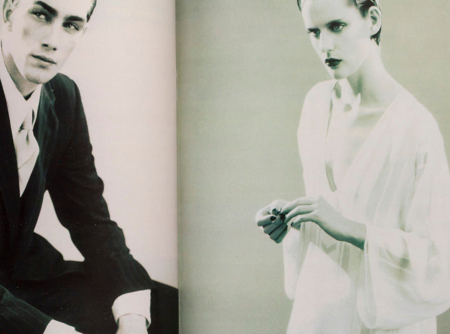 An open book or magazine spread showing two vintage fashion photographs on the pages: a seated man in a dark suit on the left and a woman in a light dress on the right, photographed against a white background.
