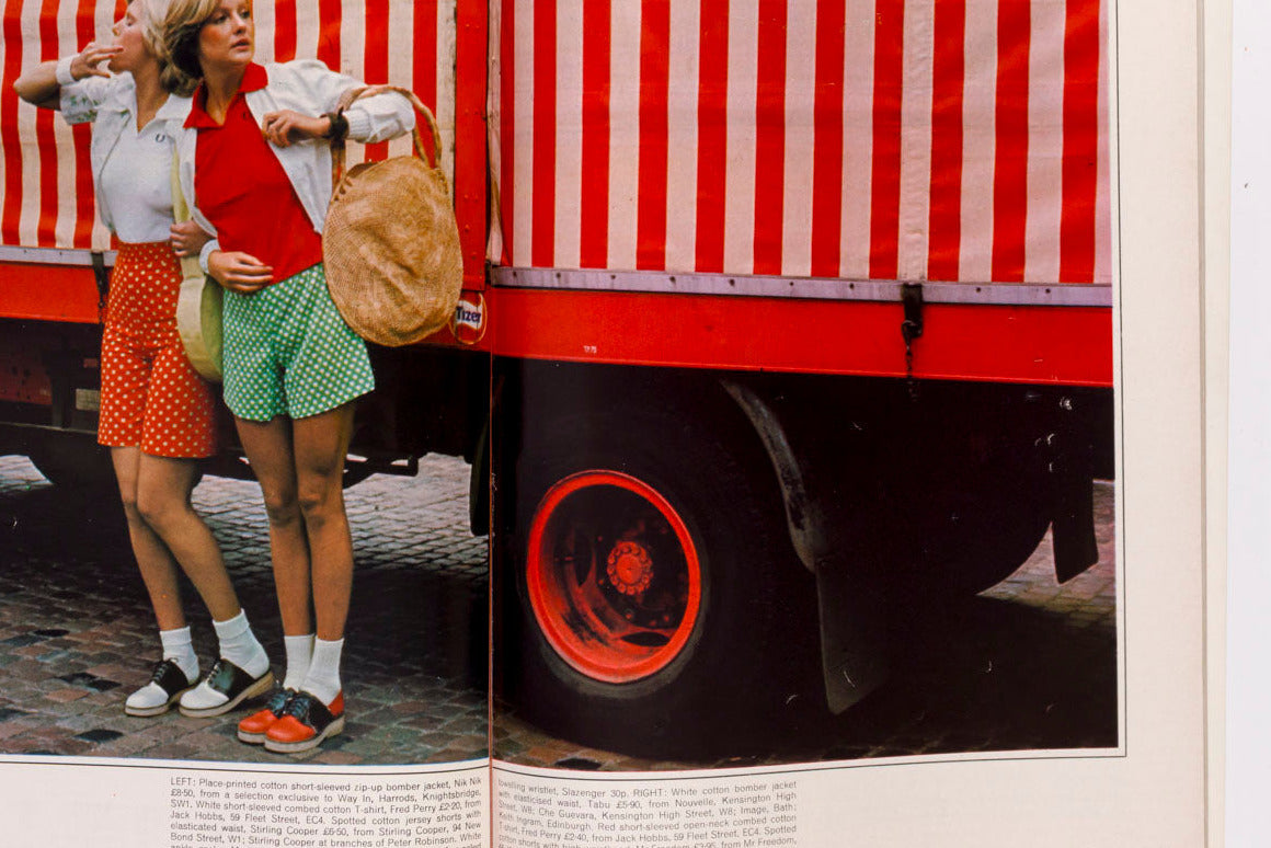 An open book or magazine spread showing a vintage-style photograph of two women standing in front of a red-and-white striped truck. The photo is printed on cream pages with small blocks of text below the image.